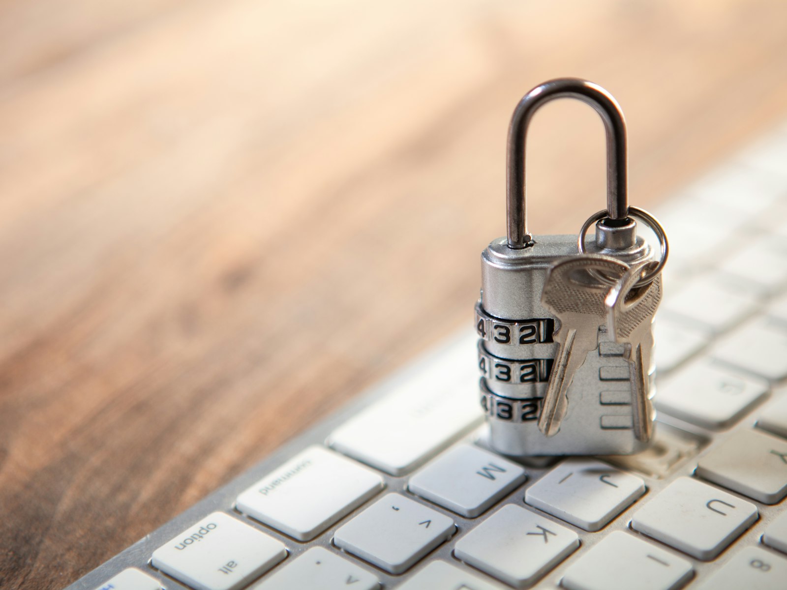 A padlock and keys resting on a keyboard on a wooden desk.